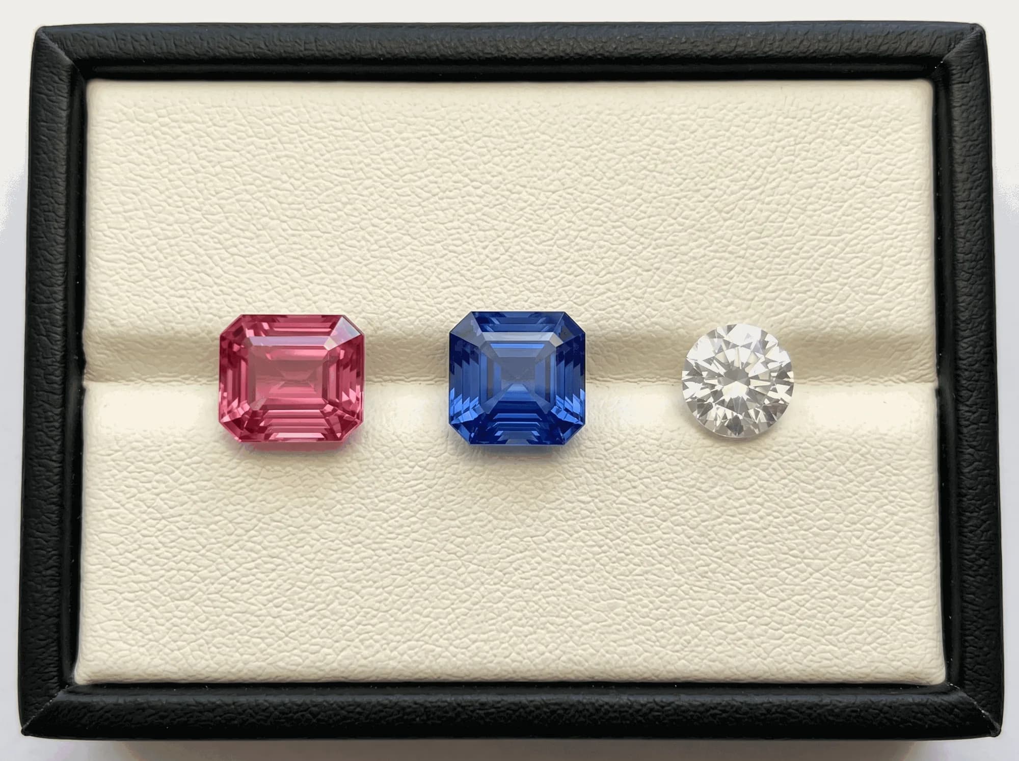 Three cut Ceylon sapphires, pink, blue and white, on a cream gem tray in a black case